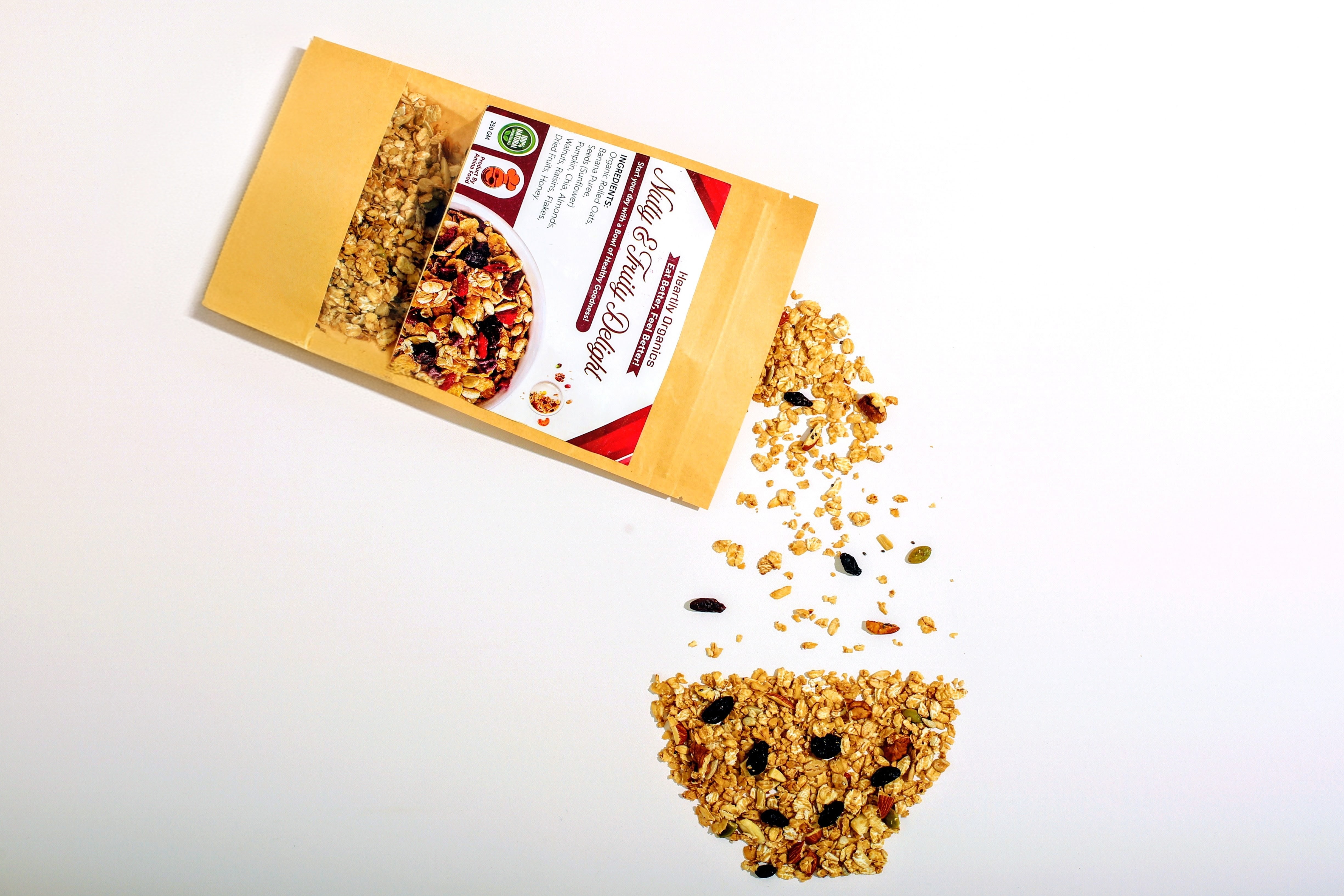 Healthy granola mix spilling from a kraft paper pouch with nuts and dried fruits